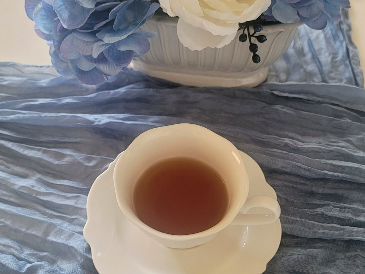 White teacup with tea beside Bloom and Grace blue and cream florals