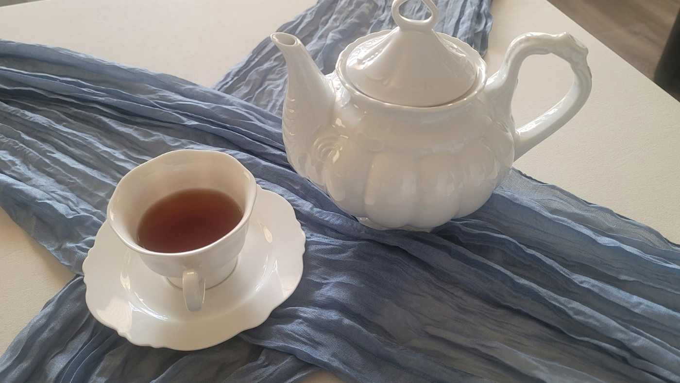 Bloom and Grace white teapot and filled teacup on dusty blue linen